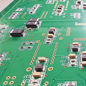 Close up of a green circuit board, many black electrical components and holes.