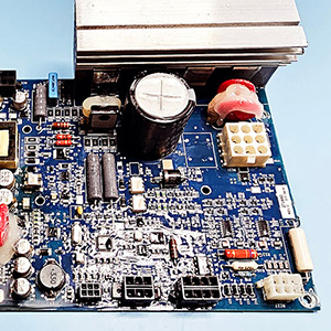 A blue circuitboard with many small components and a large black capacitor at the top.